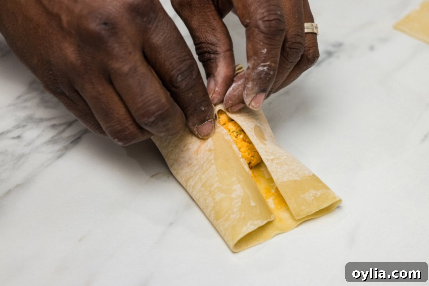 Further step of hands rolling the egg roll wrapper over the filling