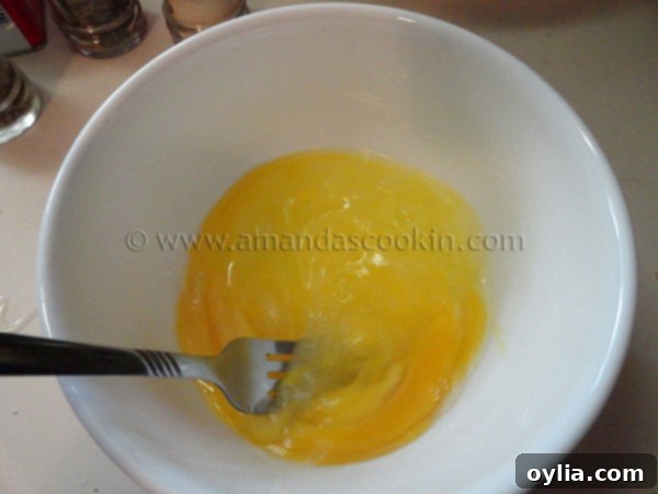 A white bowl filled with three thoroughly whisked large eggs, ready for the breading process.