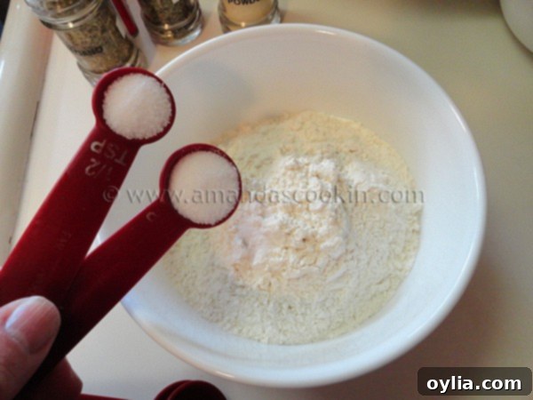 A hand adding a pinch of salt to a bowl of all-purpose flour, preparing the dry coating for the chicken nuggets.