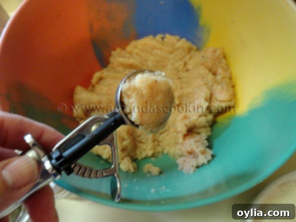 A stainless steel cookie scoop filled with a perfectly rounded portion of raw chicken paste, ready for shaping.