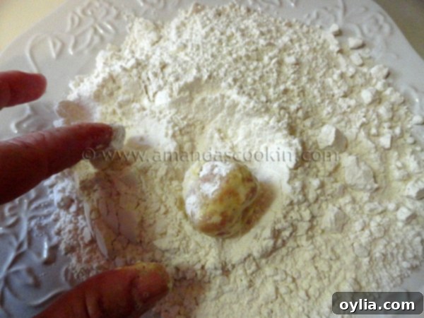 The egg-coated chicken ball being rolled again in the flour mixture, creating a double-coated breading.
