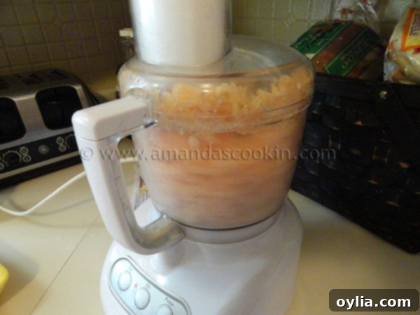 Cubed raw boneless, skinless chicken breasts inside a food processor bowl, ready for grinding.