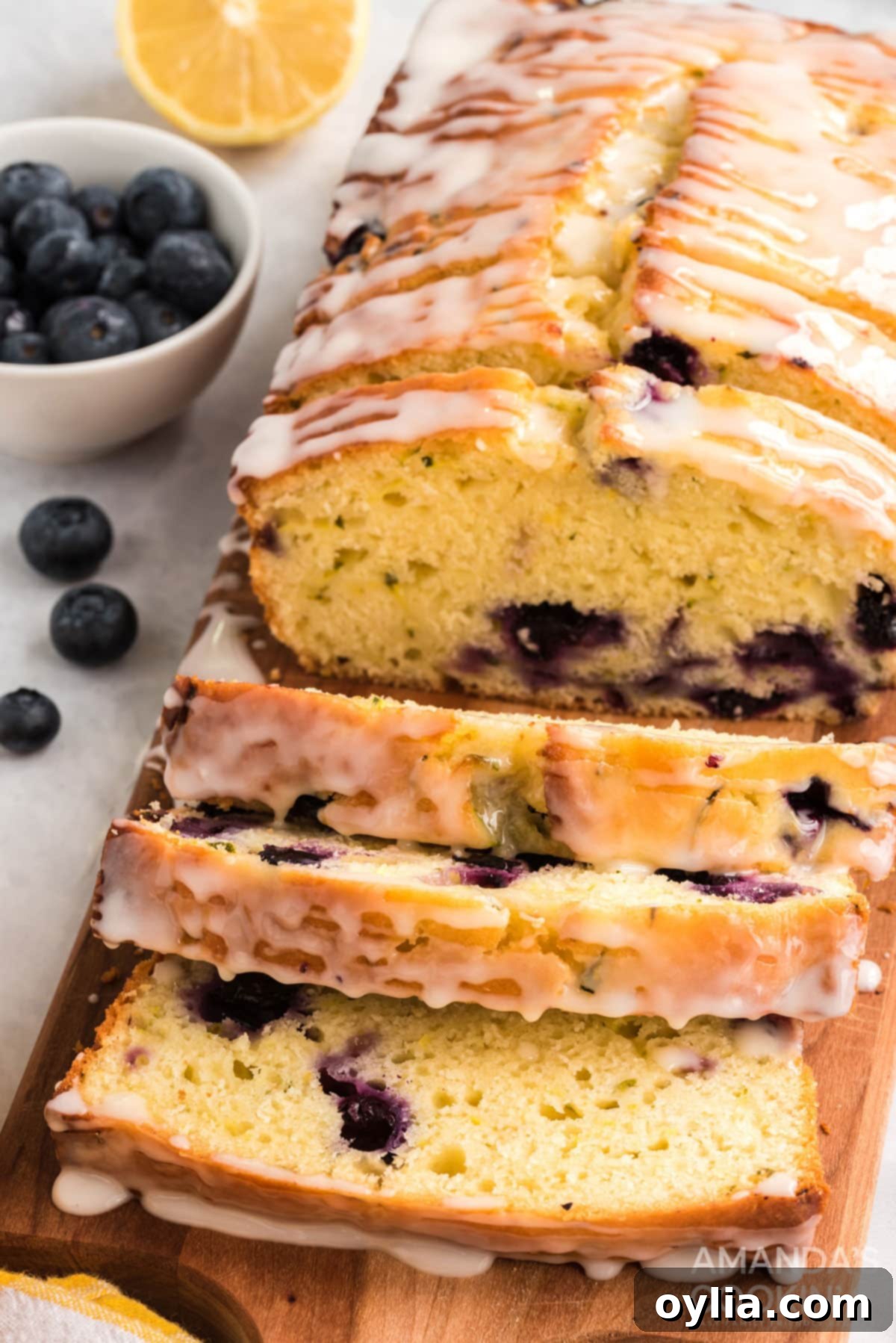Close up of a perfectly sliced Lemon Blueberry Zucchini Bread revealing blueberries and moist texture, drizzled with lemon glaze