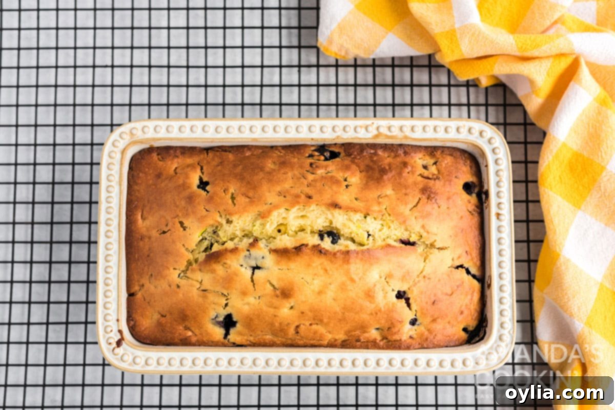 Freshly baked lemon zucchini bread cooling in its loaf pan on a wire rack.