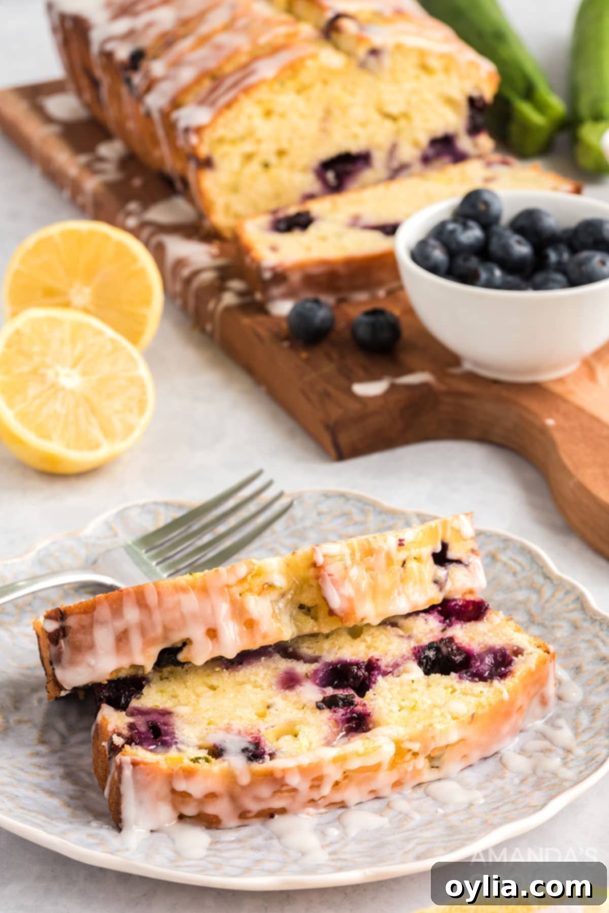 Two generous slices of Lemon Blueberry Zucchini Bread with glaze on a white plate, ready to be served.