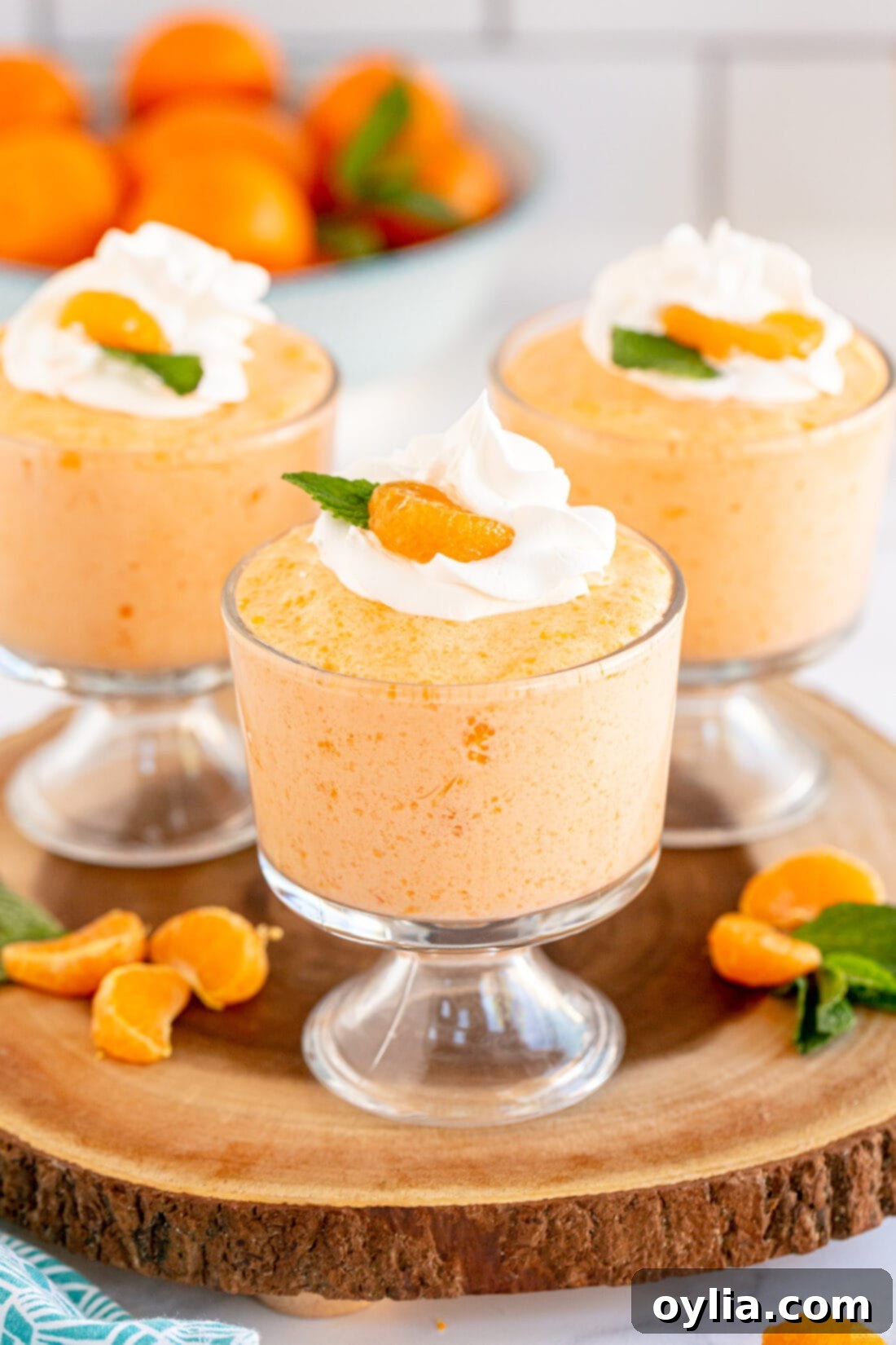 Three individual dessert cups filled with light and airy whipped Jello Mandarin Orange Mousse, each garnished with a fresh mandarin orange segment and a swirl of whipped cream.
