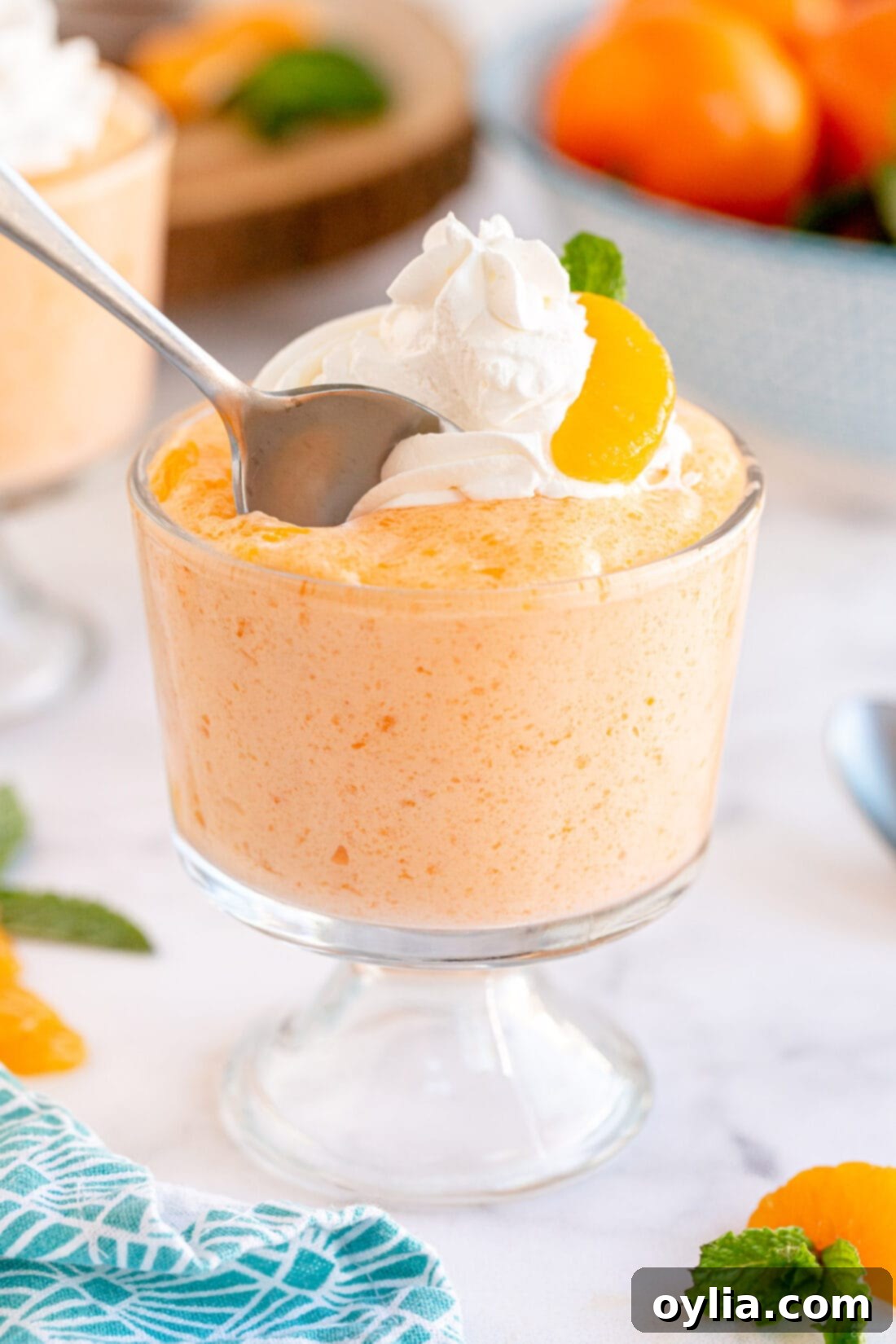 A spoon scooping into a cup of fluffy whipped Jello Mandarin Orange Mousse, highlighting its light and airy texture.