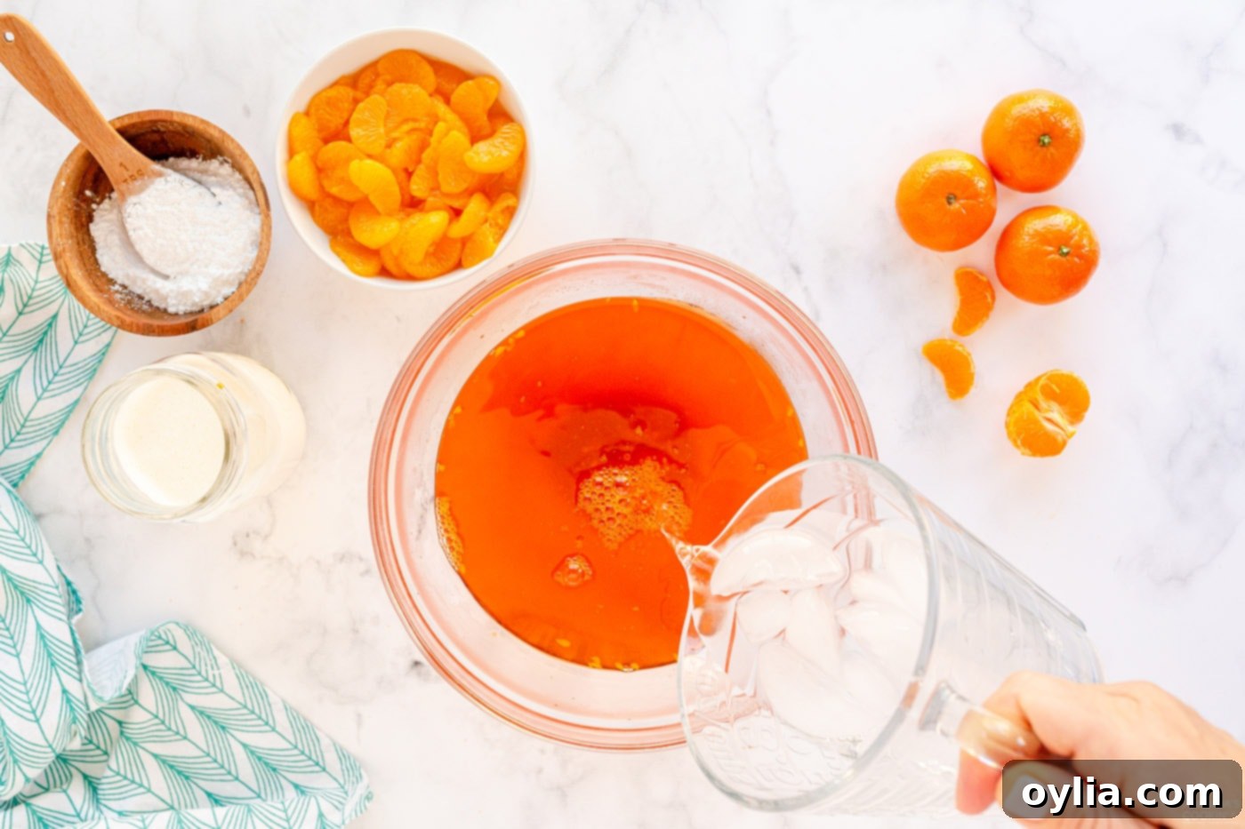 A hand pouring ice water into a bowl of warm gelatin mixture, stirring to cool it down quickly.