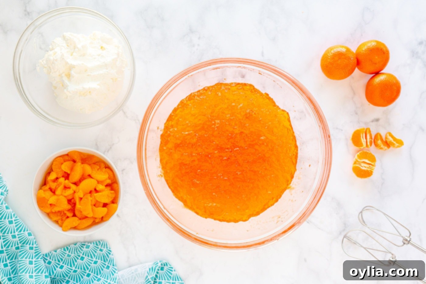 A bowl of partially set Jello mixture being whipped with an electric mixer until it becomes loose, light, and foamy.