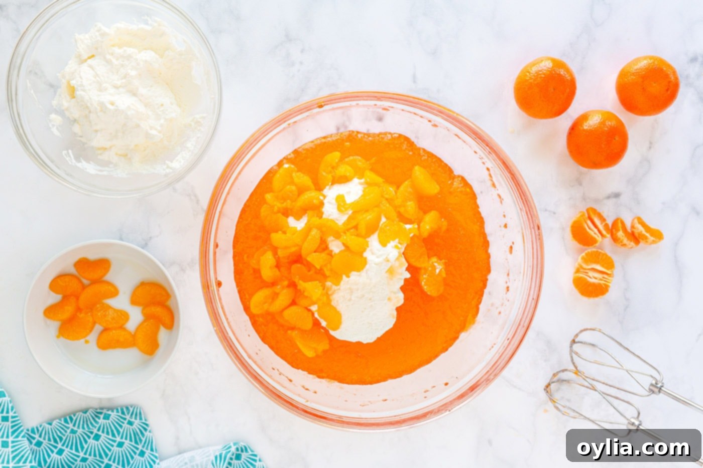 All ingredients for mandarin orange mousse – whipped Jello, whipped cream, and mandarin oranges – perfectly blended in a large mixing bowl, creating a fluffy and creamy texture.
