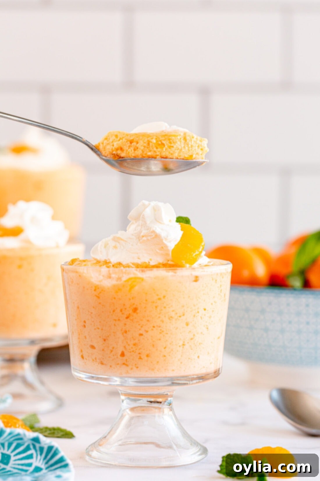 A close-up of a spoon scooping into a serving of light and fluffy whipped Jello Mandarin Orange Mousse, showcasing its creamy texture and embedded mandarin orange pieces.