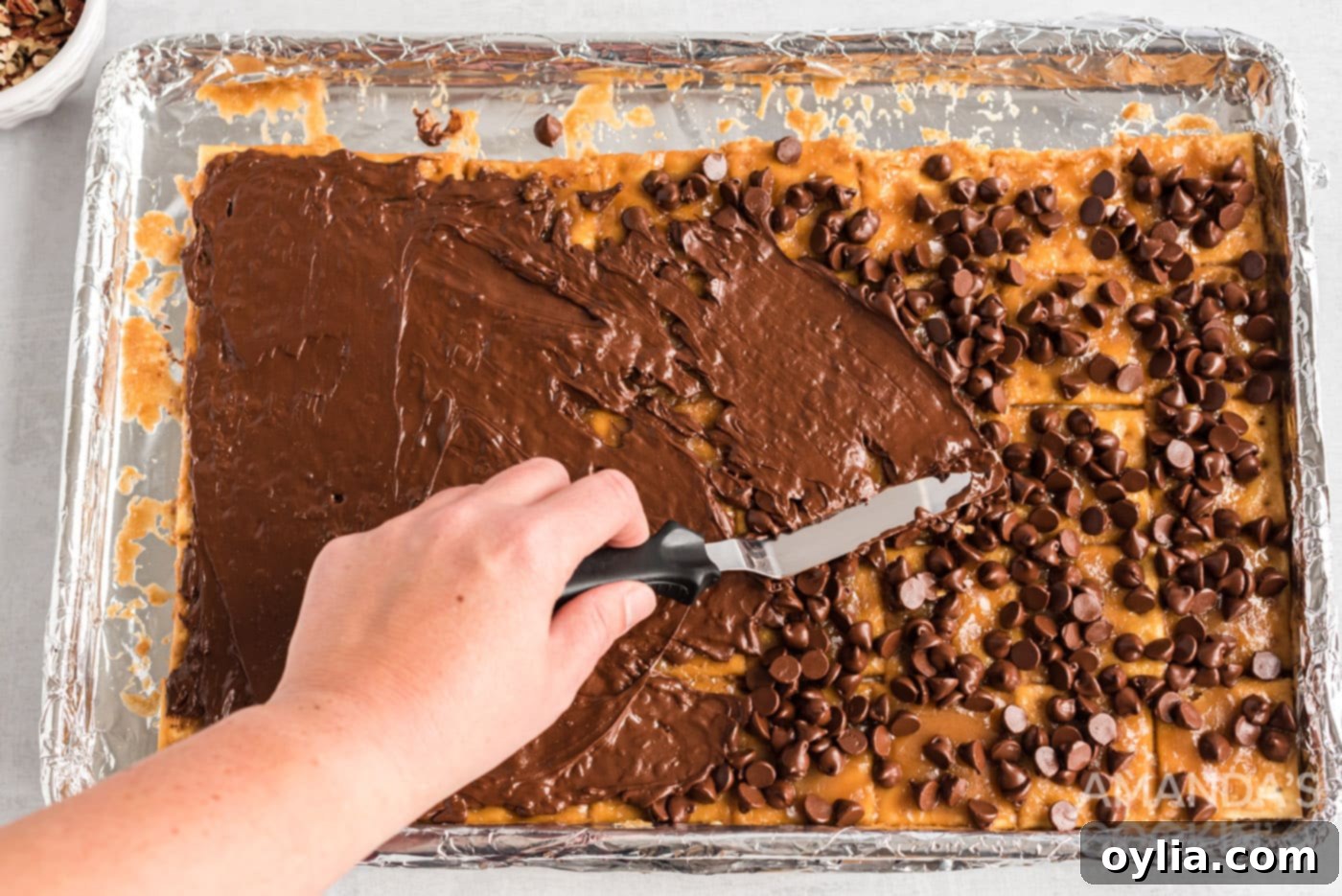 spatula spreading melted chocolate over saltine toffee