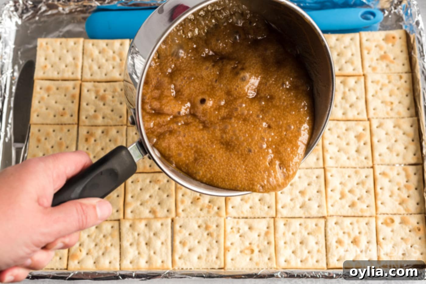 pouring caramel over saltine crackers on a baking sheet