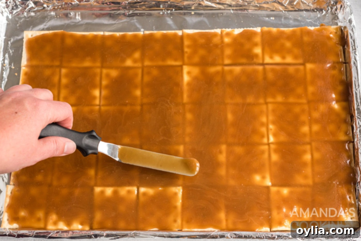 spatula spreading caramel over saltine crackers