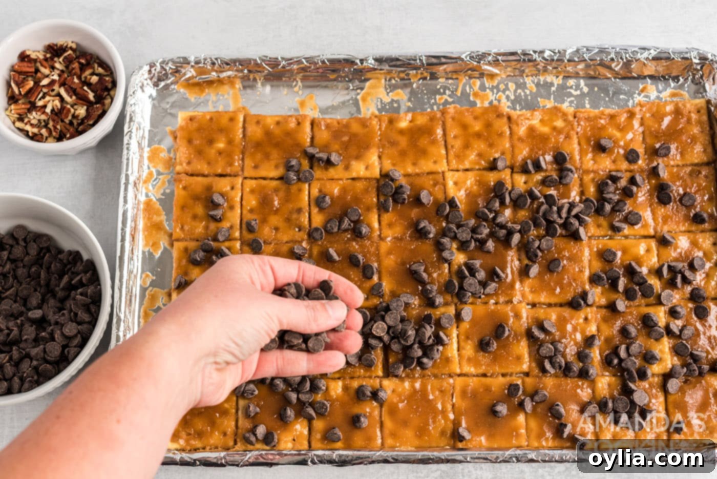 hand sprinkling chocolate chips onto caramel crackers