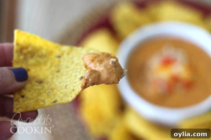 A tortilla chip generously loaded with rich chili cheese dip, ready for a delicious bite.