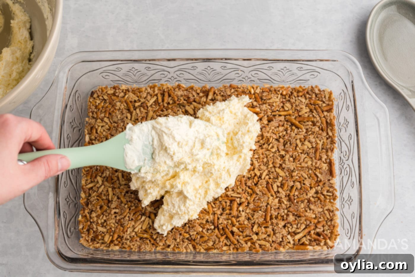 spreading cream cheese layer on top of a pretzel crust