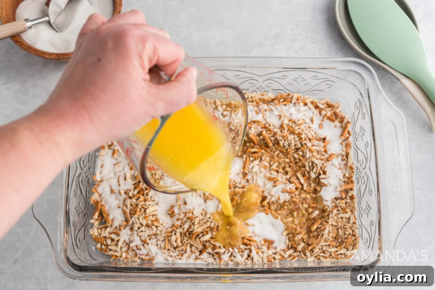 adding melted butter to pretzels and sugar in a baking pan