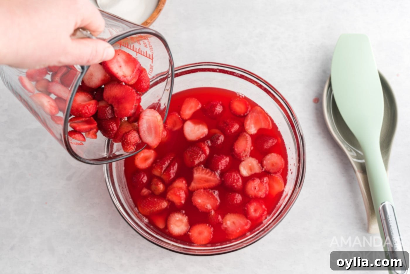 pouring sliced strawberries into a dish with gelatin