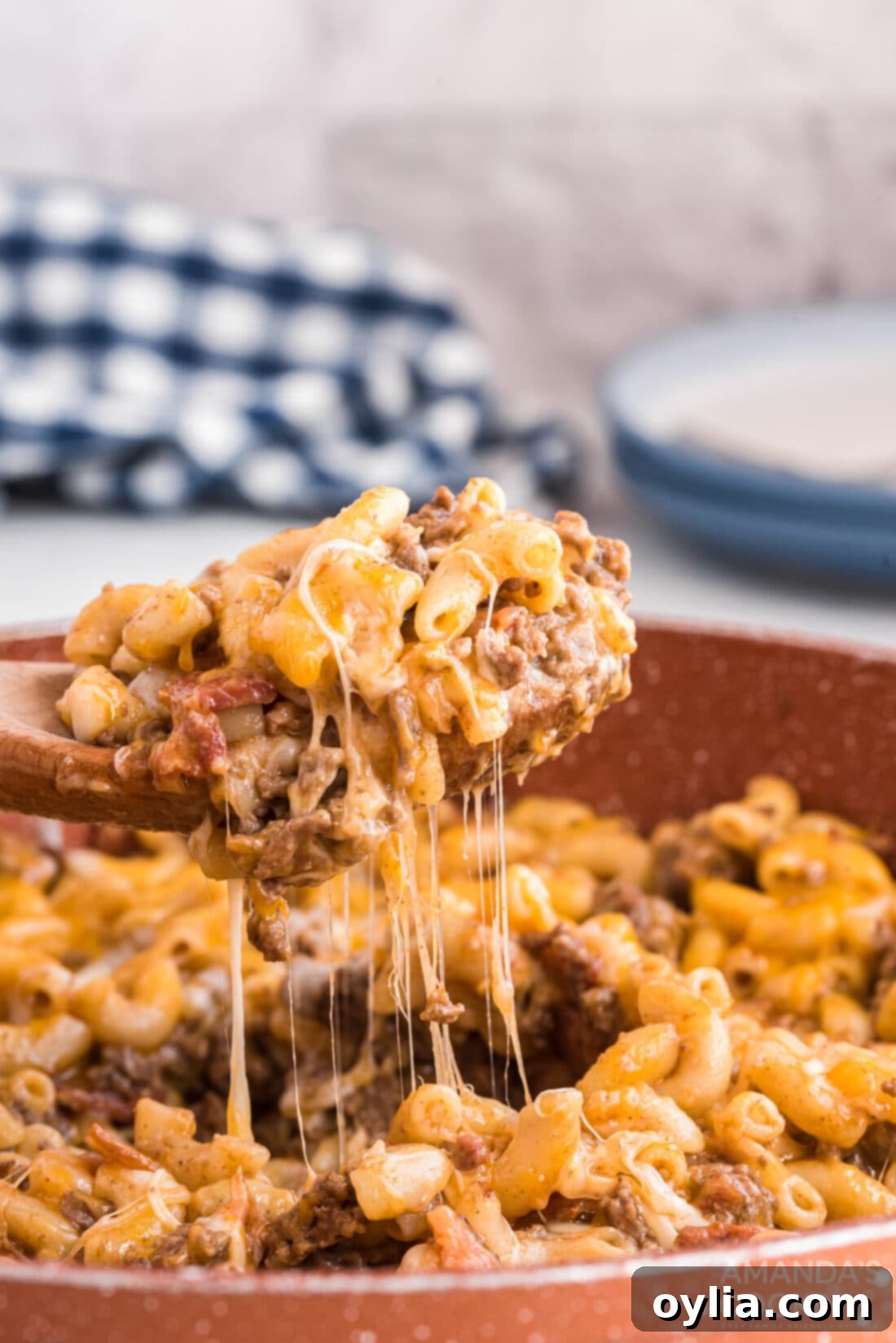 Lifting a spoon of Bacon Cheeseburger Casserole from a skillet, showing cheesy pasta, ground beef, and bacon bits
