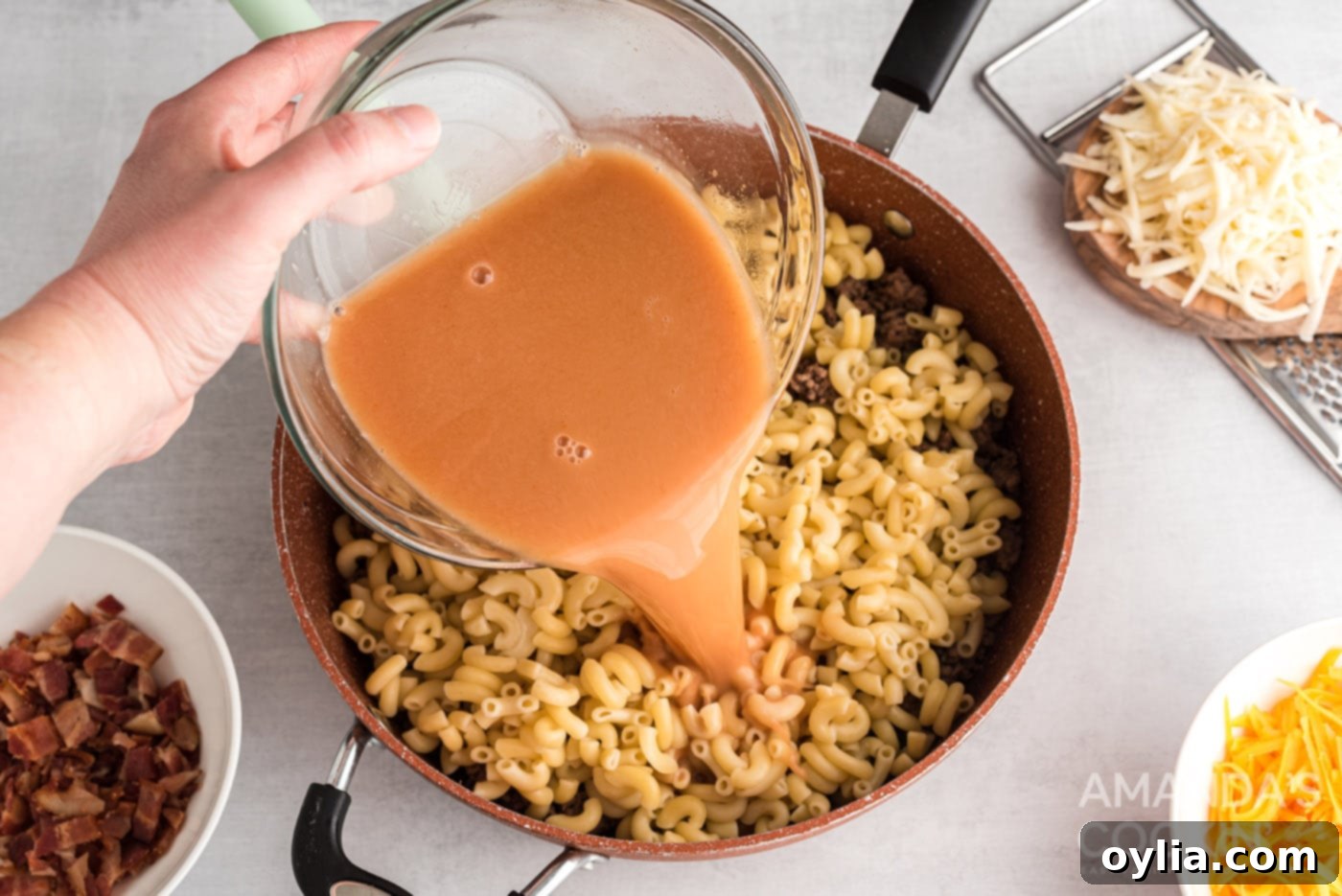 Pouring the beef broth mixture over the pasta and ground beef in the skillet, before stirring