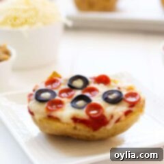 A close up of a baked potato pizza on  white plate topped with pepperoni and black olives.