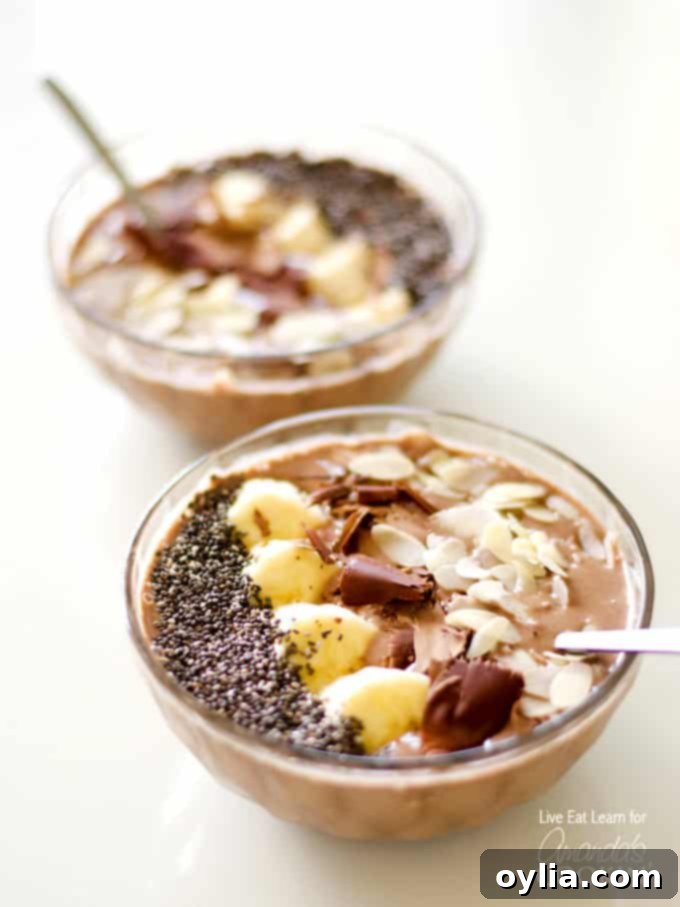 A close up of two mocha smoothie bowls topped with sliced banana, shaved chocolate and sliced almonds.