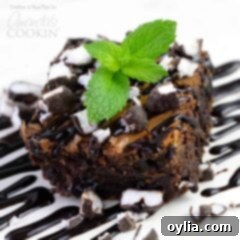 A close up photo of a peppermint patty brownie topped with drizzled chocolate sauce, chopped peppermint patties and a mint leaf.