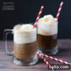 A photo of two root beer float cocktails in clear mugs served with a red and white striped straw.
