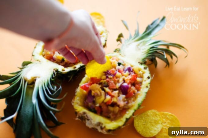 A close-up photo of a crispy tortilla chip delicately scooping fresh pineapple salsa from a natural pineapple serving boat.