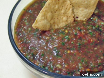 A close-up photo of classic red salsa in a clear bowl with two tortilla chips dipped in, ready to eat.