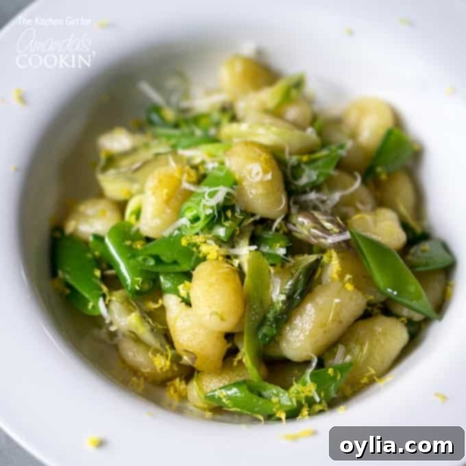 A close up overhead photo of pan seared gnocchi with shaved asparagus and snap peas in a white bowl.
