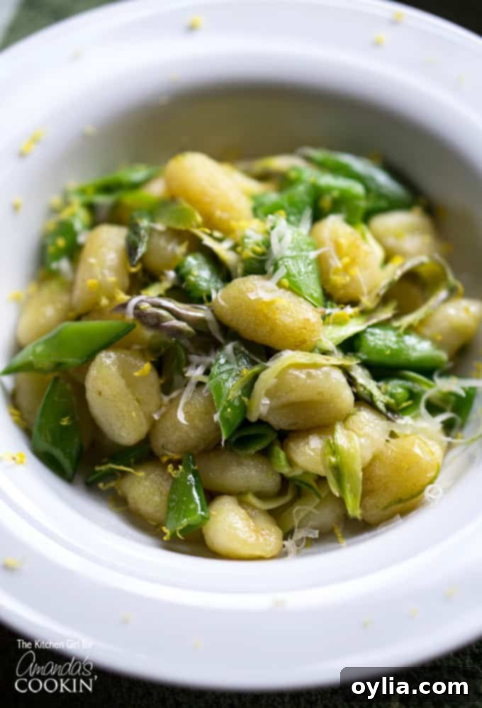 A close up overhead photo of pan seared gnocchi with shaved asparagus and snap peas in a white bowl.