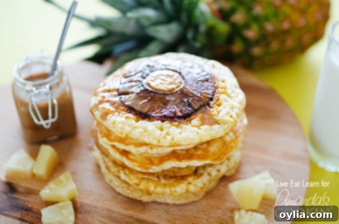 A beautifully arranged stack of Pineapple Pancakes, generously drizzled with homemade coconut syrup, on a rustic wooden board.