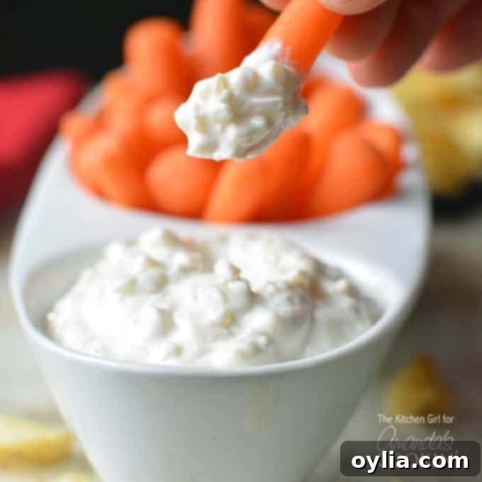 A close up of a carrot dipped in skinny French onion dip with dip and carrots in a serving dish in the background.