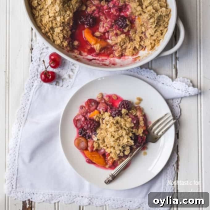 An overhead photo of a serving of summer fruit crisp on a plate with a fork and the entire pan behind it.