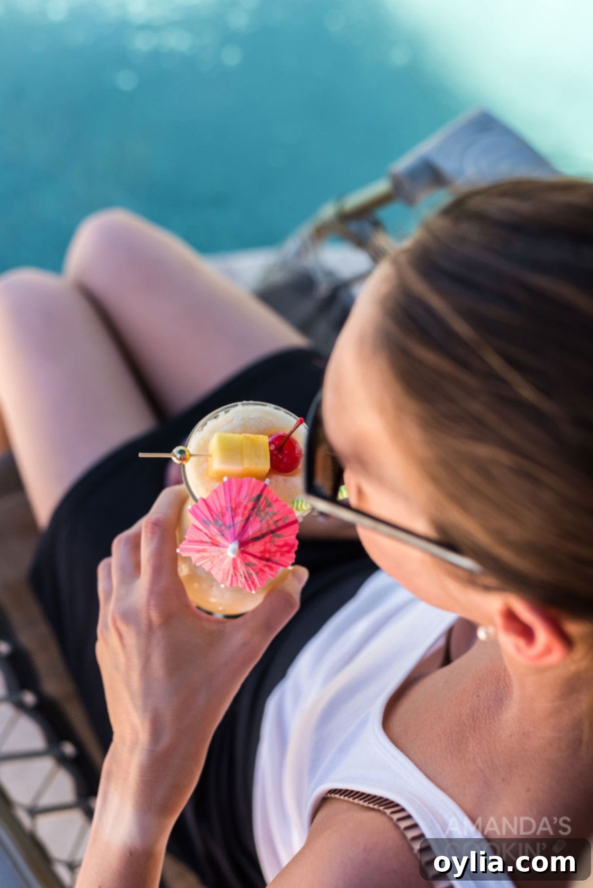 Woman happily sipping on a refreshing Pina Colada by the pool on a beautiful day.