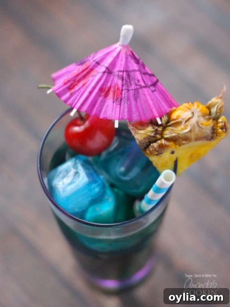 A tall glass filled with a blue mermaid cocktail and topped with a cherry, pineapple wedge, an umbrella and a straw.