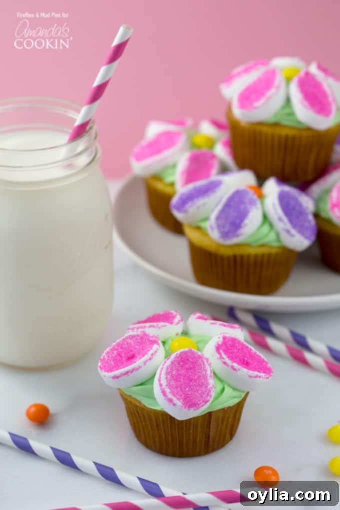 A photo of marshmallow flower cupcakes with a glass of milk to the side.