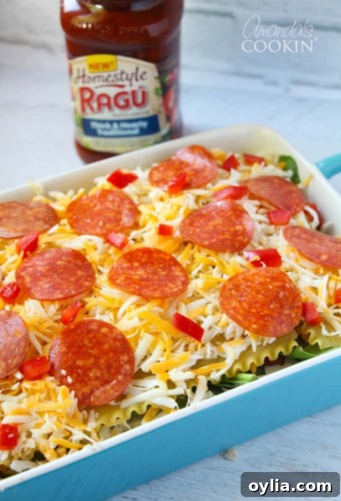 A close up photo of an unbaked pizza lasagna in a blue casserole dish, topped with cheese and pepperoni, before going into the oven.