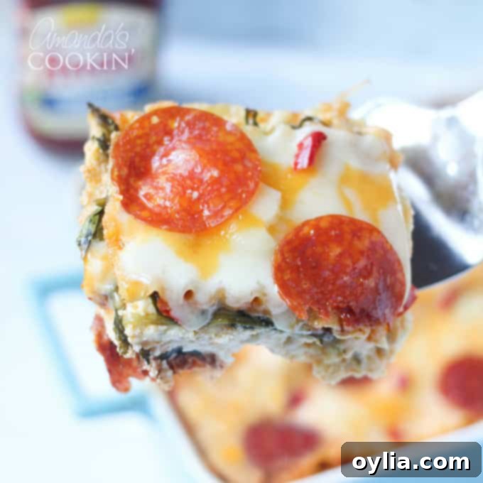 A close up photo of a serving of pizza lasagna being lifted with a spatula, showing the cheesy, layered texture.