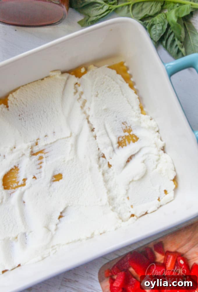 An overhead photo of lasagna noodles laid in a pan with a smooth layer of ricotta cheese spread on top, forming the first creamy layer.