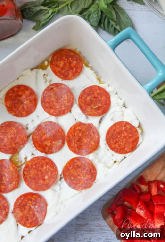 An overhead photo of lasagna noodles in a pan with ricotta cheese and an organized layer of pepperoni slices, illustrating the pizza inspiration.