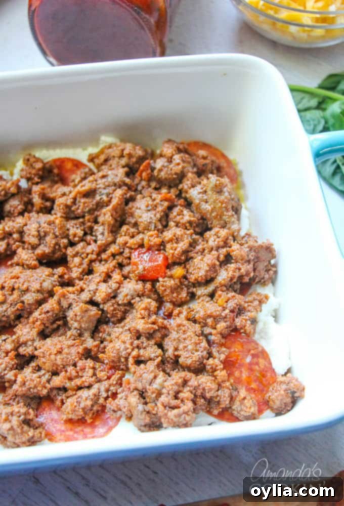 An overhead photo of cooked ground beef evenly spread over pepperoni, ricotta cheese, and lasagna noodles in a casserole dish.