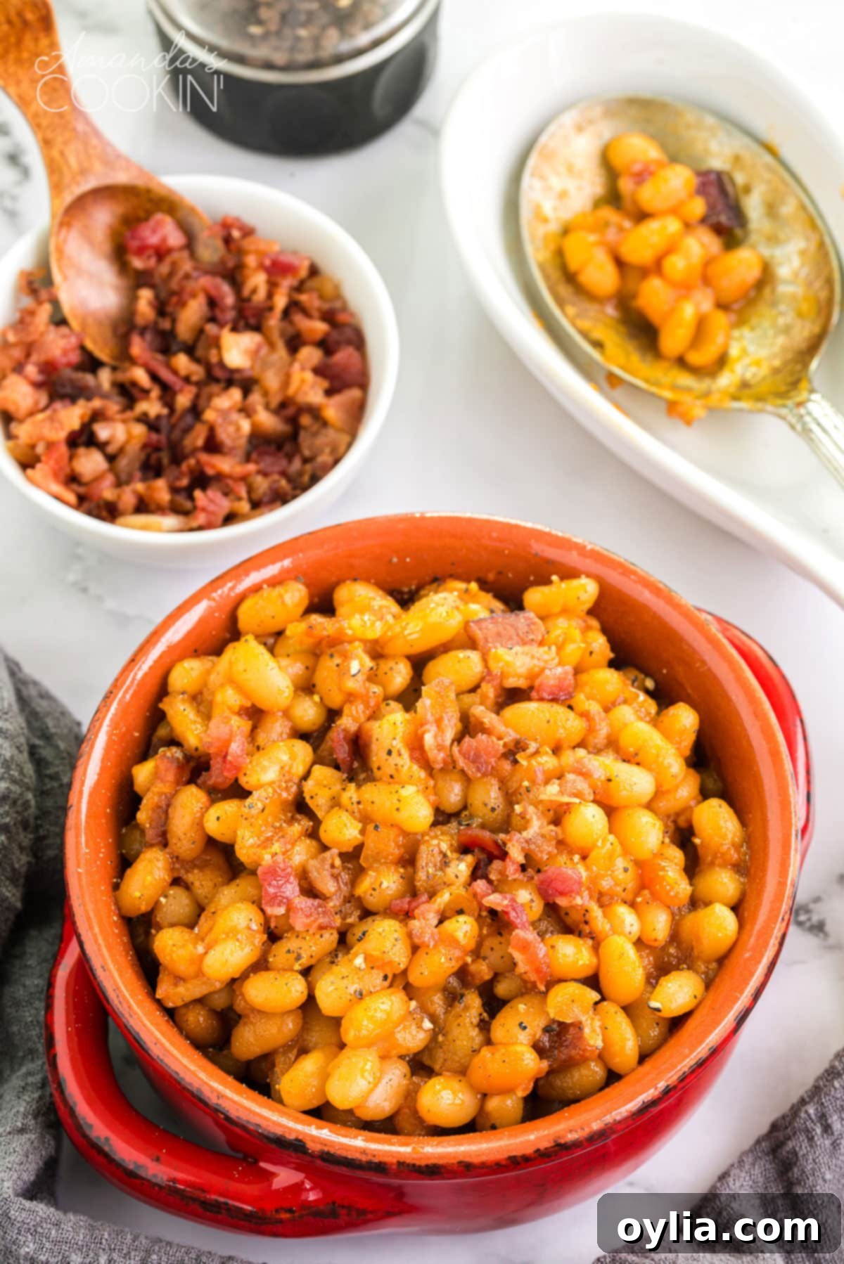 These homemade baked beans are baked in a delicious tangy sweet and savory sauce of brown sugar, maple syrup, ketchup, and apple cider vinegar. A rustic crock of homemade baked beans sits invitingly on a wooden table, ready to be served.