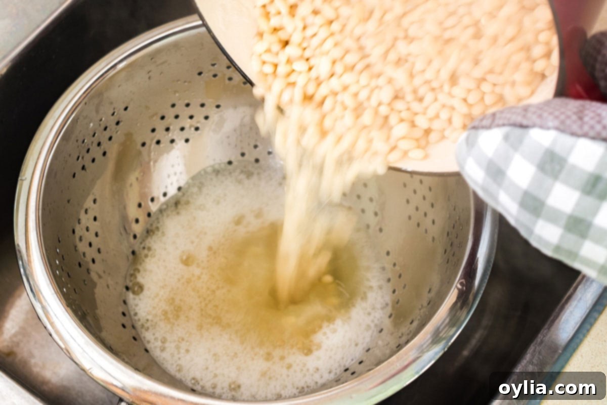 Perfectly Homemade Baked Beans 6 Draining cooked beans from a pot into a colander, with a bowl placed underneath to collect the starchy cooking liquid.
