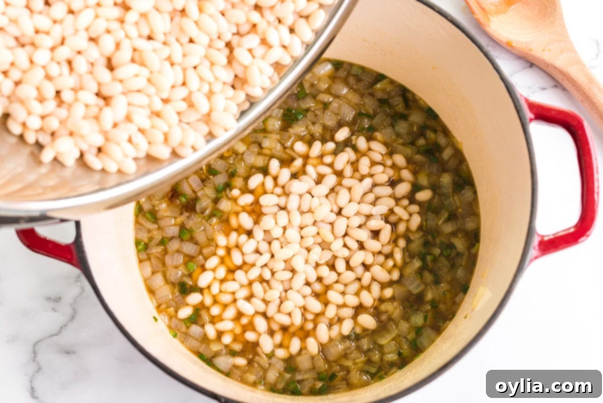 Perfectly Homemade Baked Beans 8 The drained beans being added to the sautéed onion and jalapeño mixture in a pot, about to be combined.