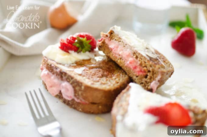 A piece of french toast with strawberries and cream, topped with powdered sugar and a fresh strawberry slice