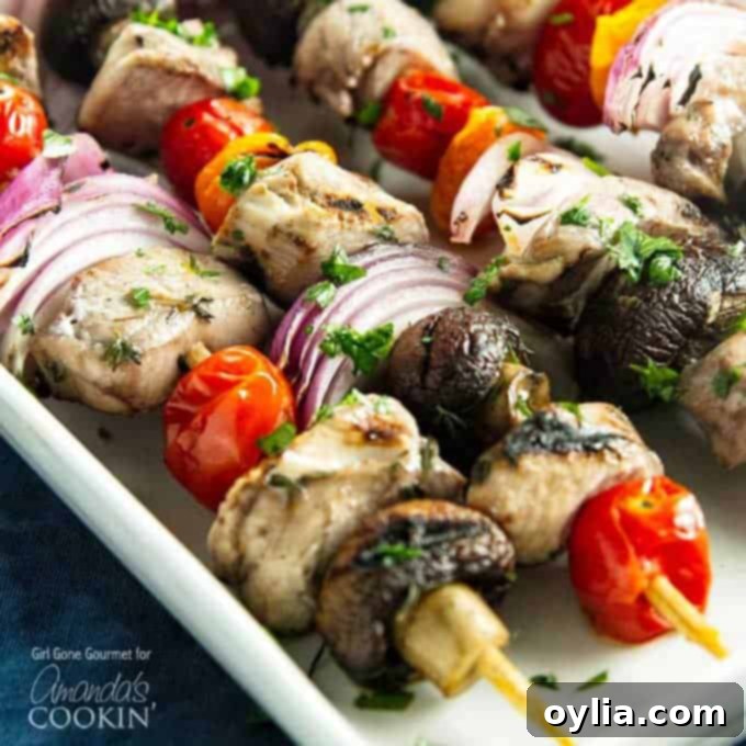 A close up of marinated chicken skewers with tomatoes, red onions and mushrooms.