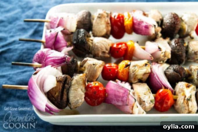 A close up of marinated chicken skewers with tomatoes, red onions and mushrooms.